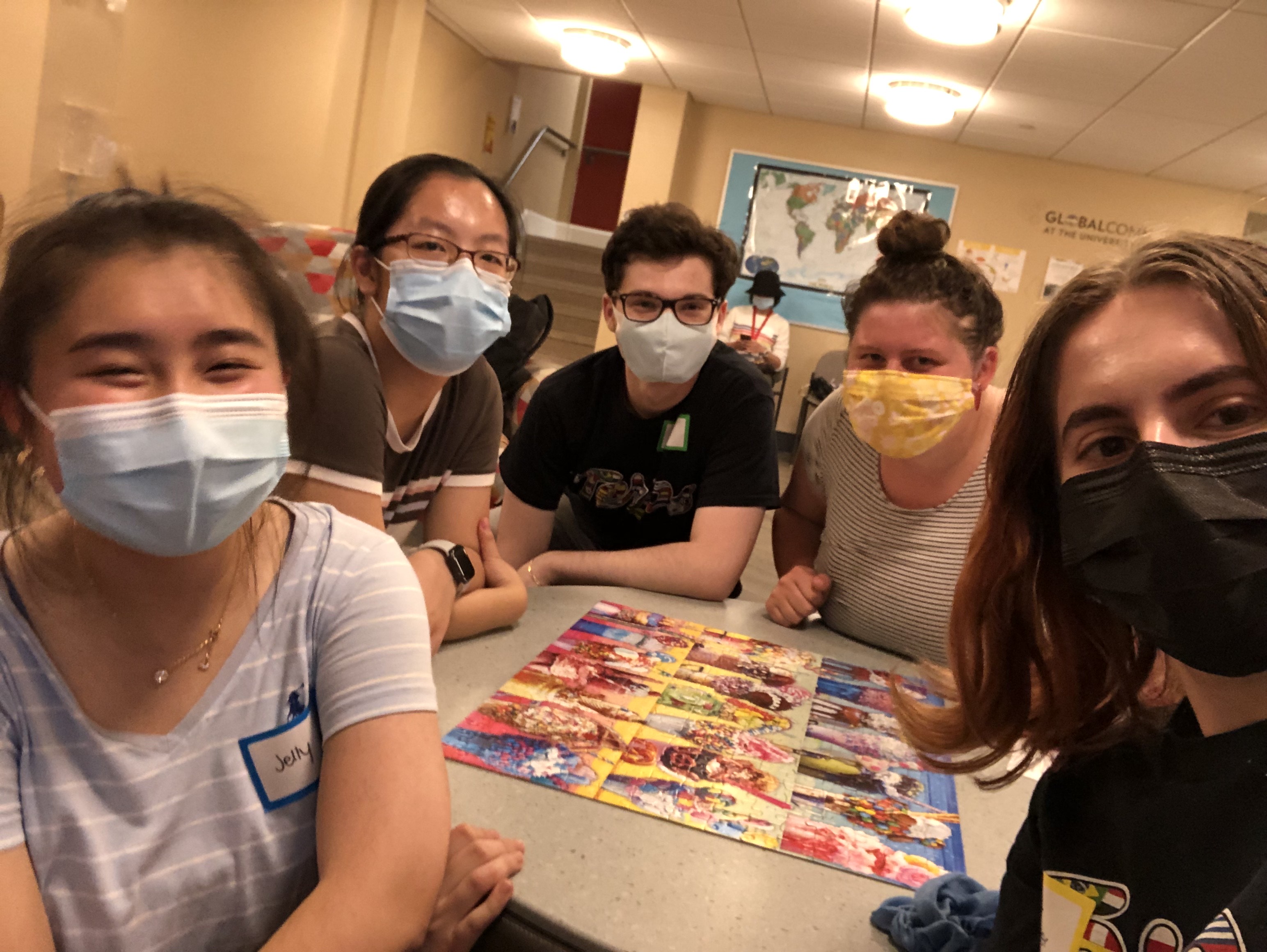 students surrounding a completed jigsaw puzzle with masks on